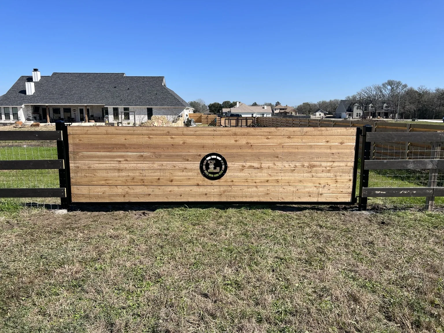 Wide custom ranch gate built with horizontal wood boards and a black steel frame